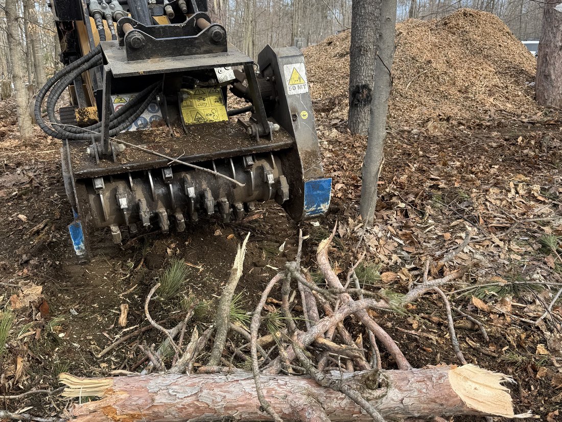 Forestry mulching head and cleared brush on a wooded lot