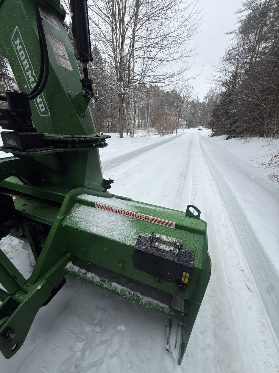 Tractor mounted snow blower clearing a rural road
