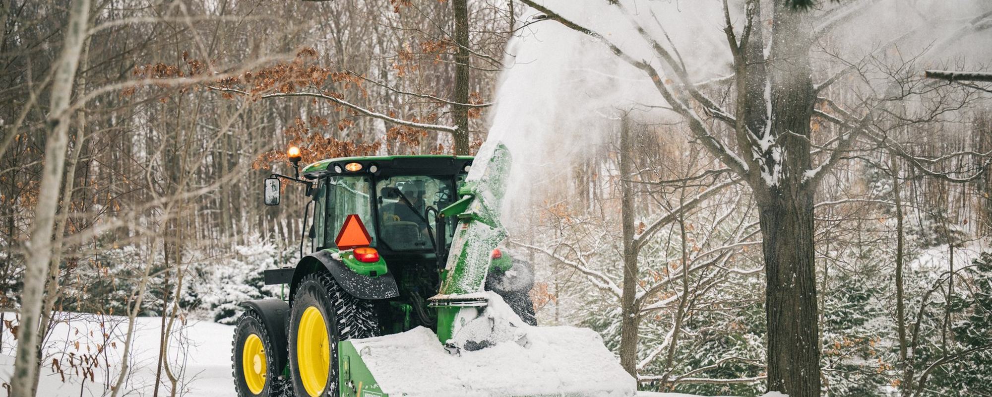 Tractor mounted snow blower clearing a rural property