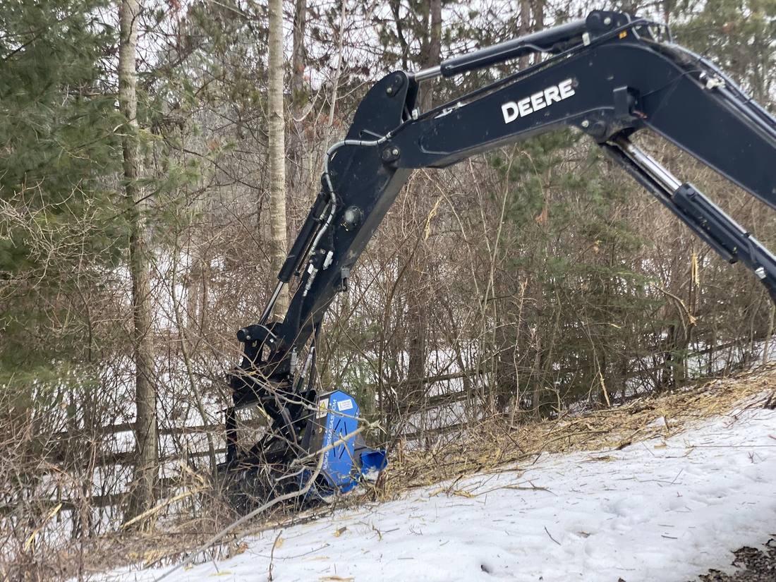 Excavator mounted mulching head clearing a fence line